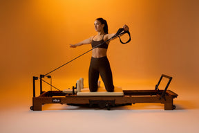 Woman exercising on a Pilates reformer machine with an orange background