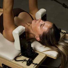 female with head and shoulders rest on beige FOLD Reformer bed