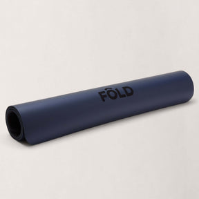 FOLD Reformer Pilates Mat - Navy rolled up showing logo on soft, durable surface, perfect for workouts.