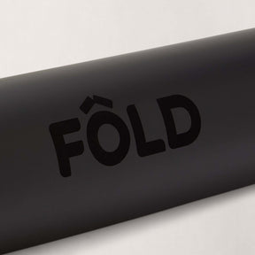 Close-up of the FOLD Yoga Mat - Black logo displayed prominently on a smooth black surface.