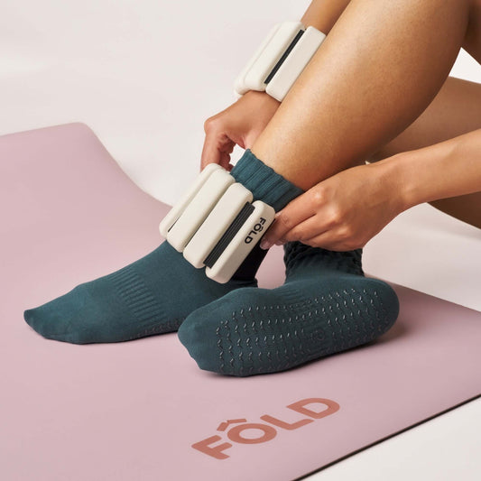 Person wearing Scrunch Grip Socks - Teal while adjusting ankle weights on a workout mat.
