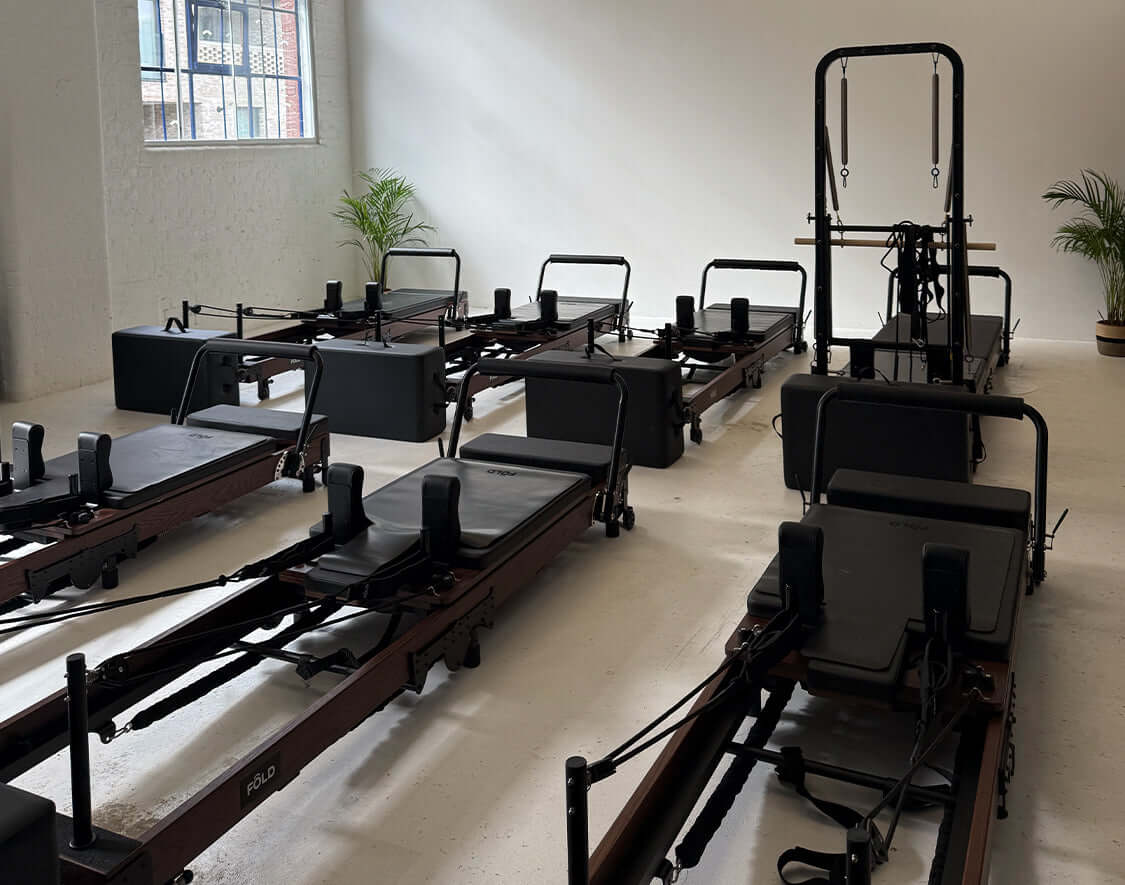 A view of multiple Studio Reformers lined up in a bright, modern studio space for fitness.