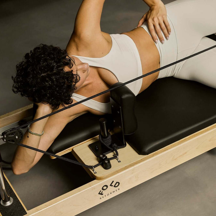 Women lying outstretched on a black FOLD Reformer bed with leg in a strap