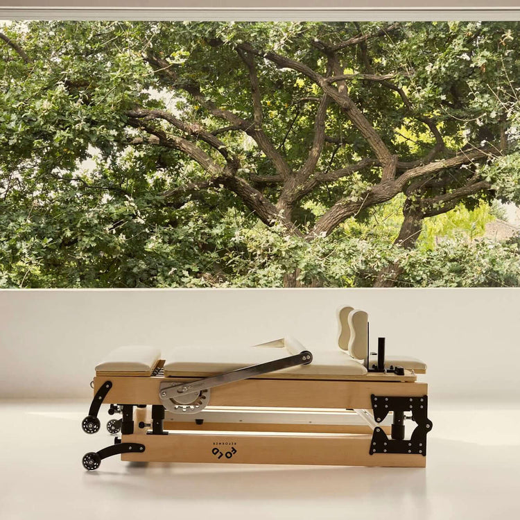 Folded FOLD Reformer bed in beige positioned in front of window with trees and leaves