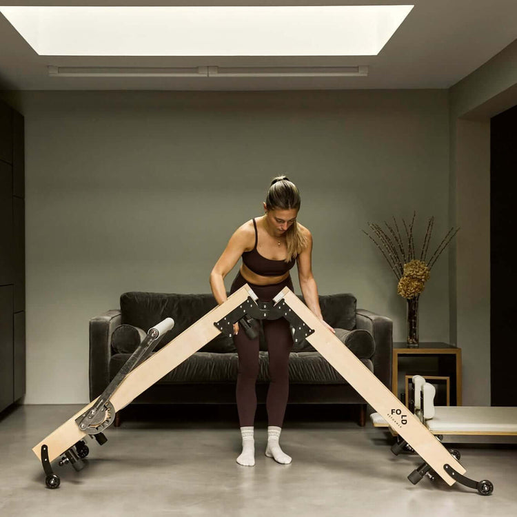 Female holding the hinges of a folding reformer bed to fold it up