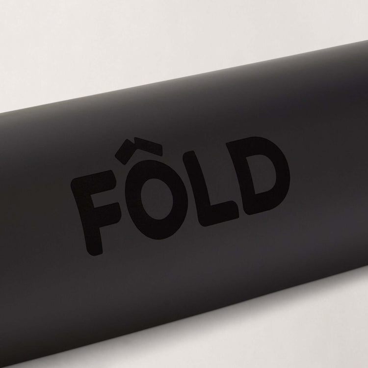 Close-up of the FOLD Yoga Mat - Black logo displayed prominently on a smooth black surface.