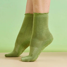 Two feet wearing green frilly Pilates socks on tip toes