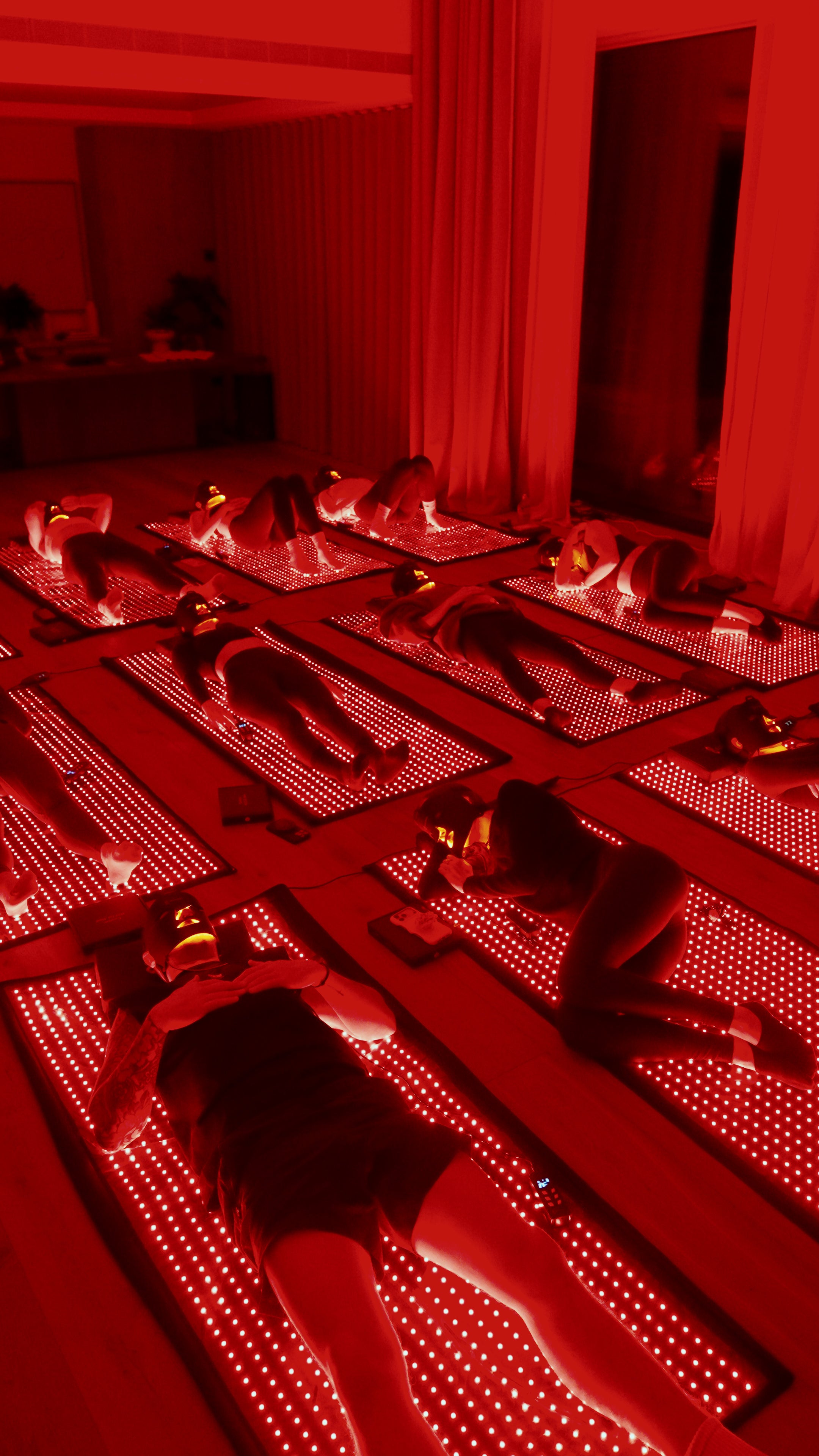 People lying on red LED mats in a dimly lit room with red lighting.